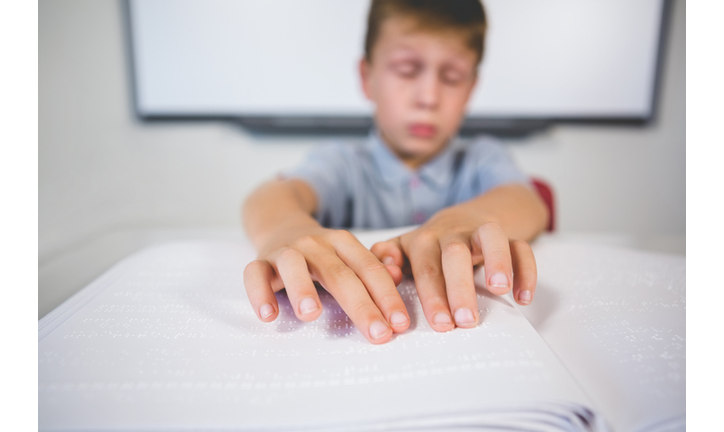 Schoolboy reading a braille book in classroom