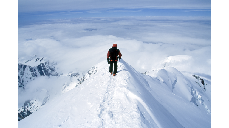 Climber on steep summit of mountain in snow.