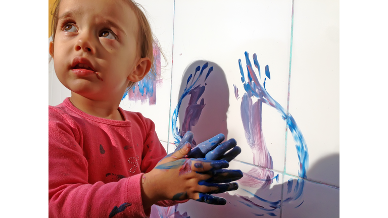 Little girl painting the wall with her hands