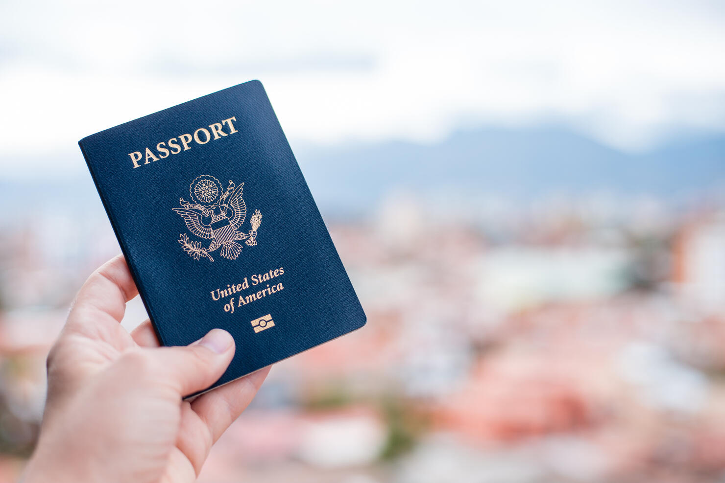 Close-Up Of Hand Holding American Passport Against Townscape