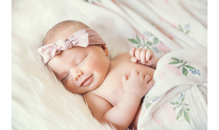 Sleeping newborn baby in a wrap on white blanket.