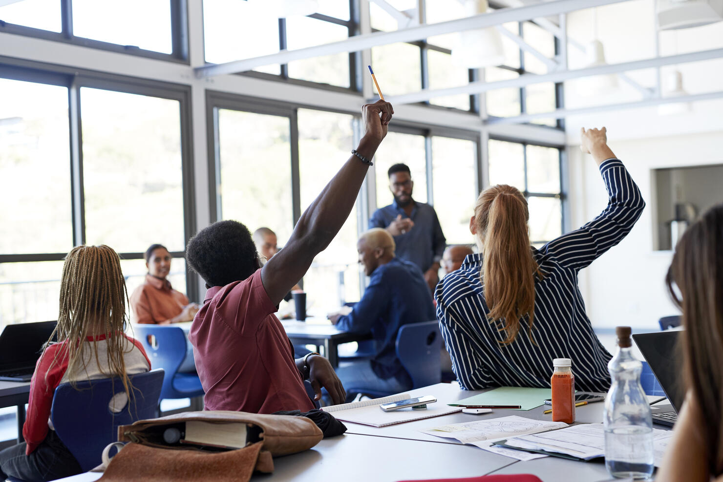 Multi-ethnic students raising hands at desk