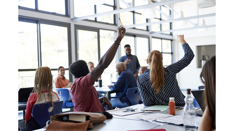 Multi-ethnic students raising hands at desk