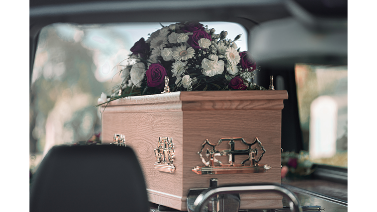 Flowers atop a coffin on display within a hearse at a funeral