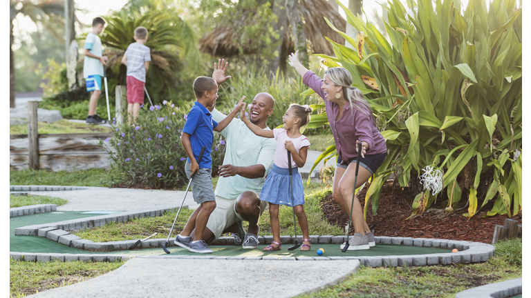 Interracial family, two children playing miniature golf