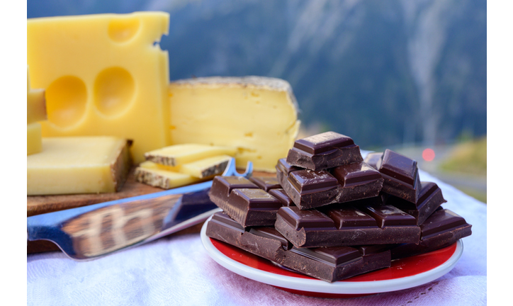 Tasty Swiss cheeses and dark pure chocolate, emmental, gruyere, appenzeller served outdoor with Alpine mountains peaks on background