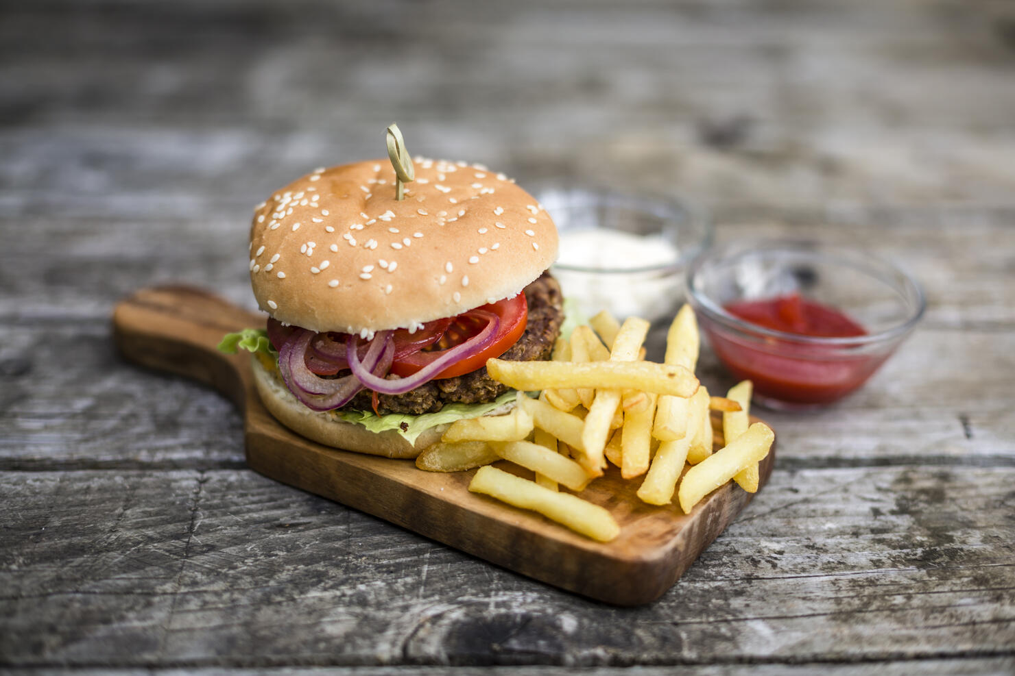 Homemade burger with lettuce, meat, tomato, onion and french fries on chopping board