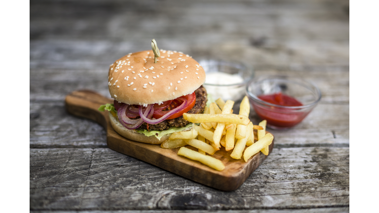Homemade burger with lettuce, meat, tomato, onion and french fries on chopping board