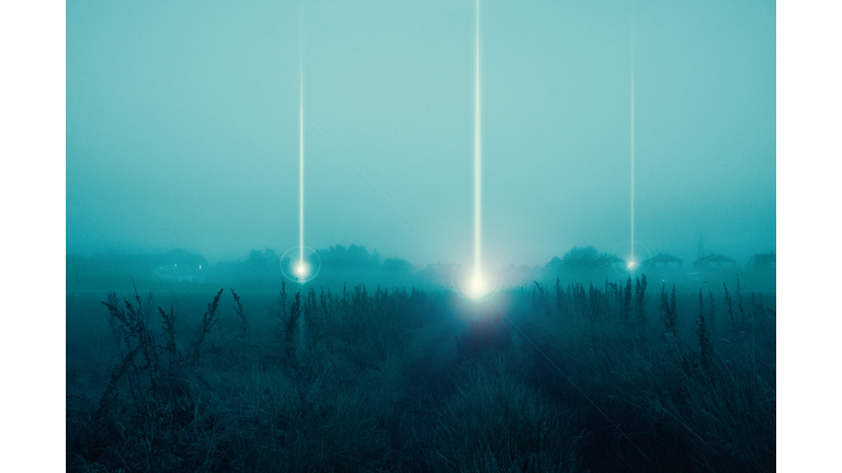 A moody science fiction concept, of UFO light beams landing in a field coming down from the sky. On a foggy spooky night.