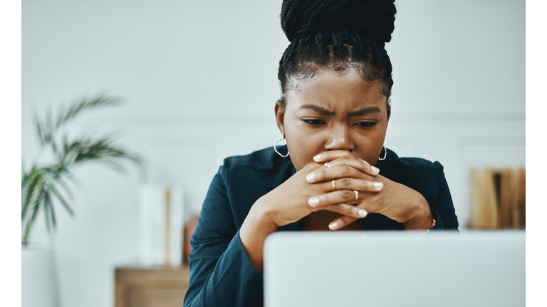 Shot of a young businesswoman frowning while using a laptop in a modern office