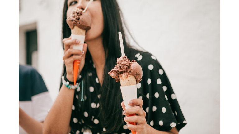 pretty latina stands on street holding melting chocolate cone ice cream