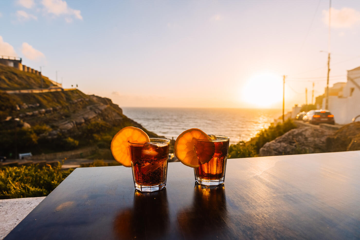 Two glasses with cocktails at the table by the ocean during sunset