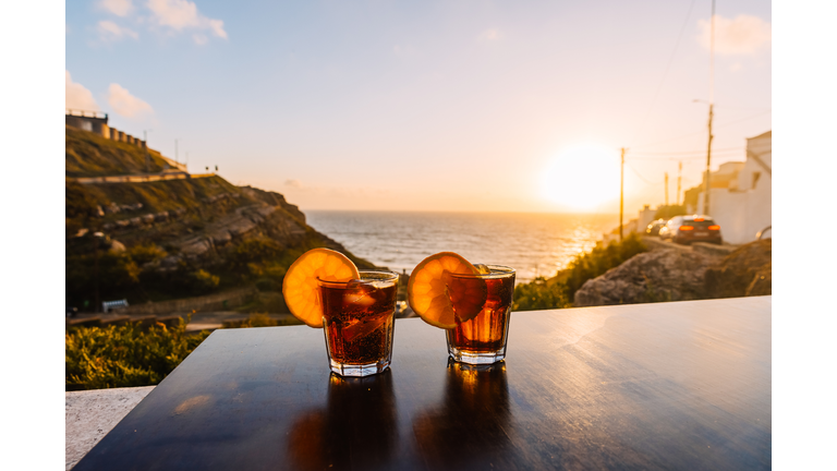 Two glasses with cocktails at the table by the ocean during sunset