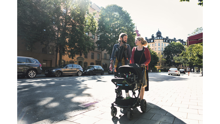 Mid adult parents with baby boy and stroller walking on sidewalk in city