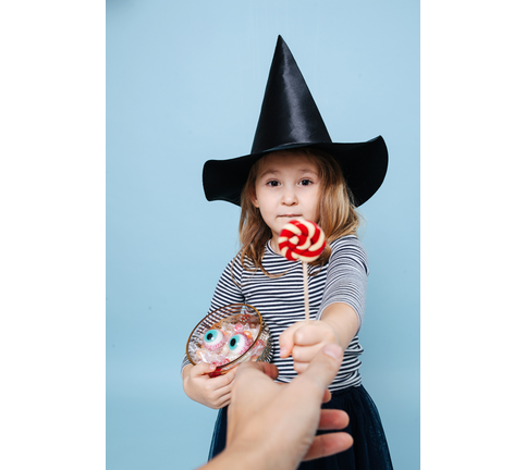 Little girl in witch hat handing away a lollipop, making puppy eyes