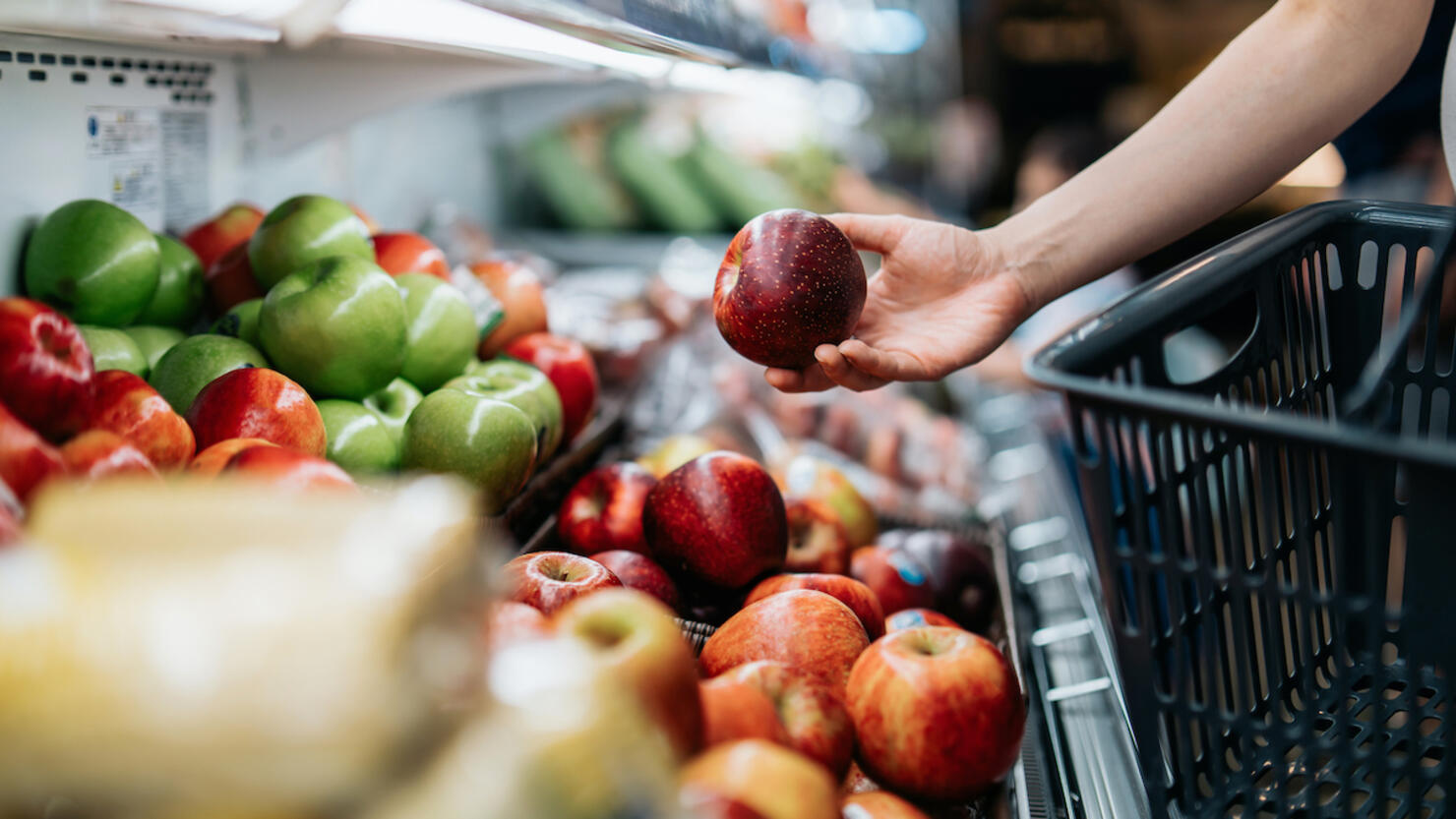 Cropped shot of young Asian woman choosing fresh organic fruits in supermarket. She is picking a red apple along the produce aisle. Routine grocery shopping. Healthy living and eating lifestyle