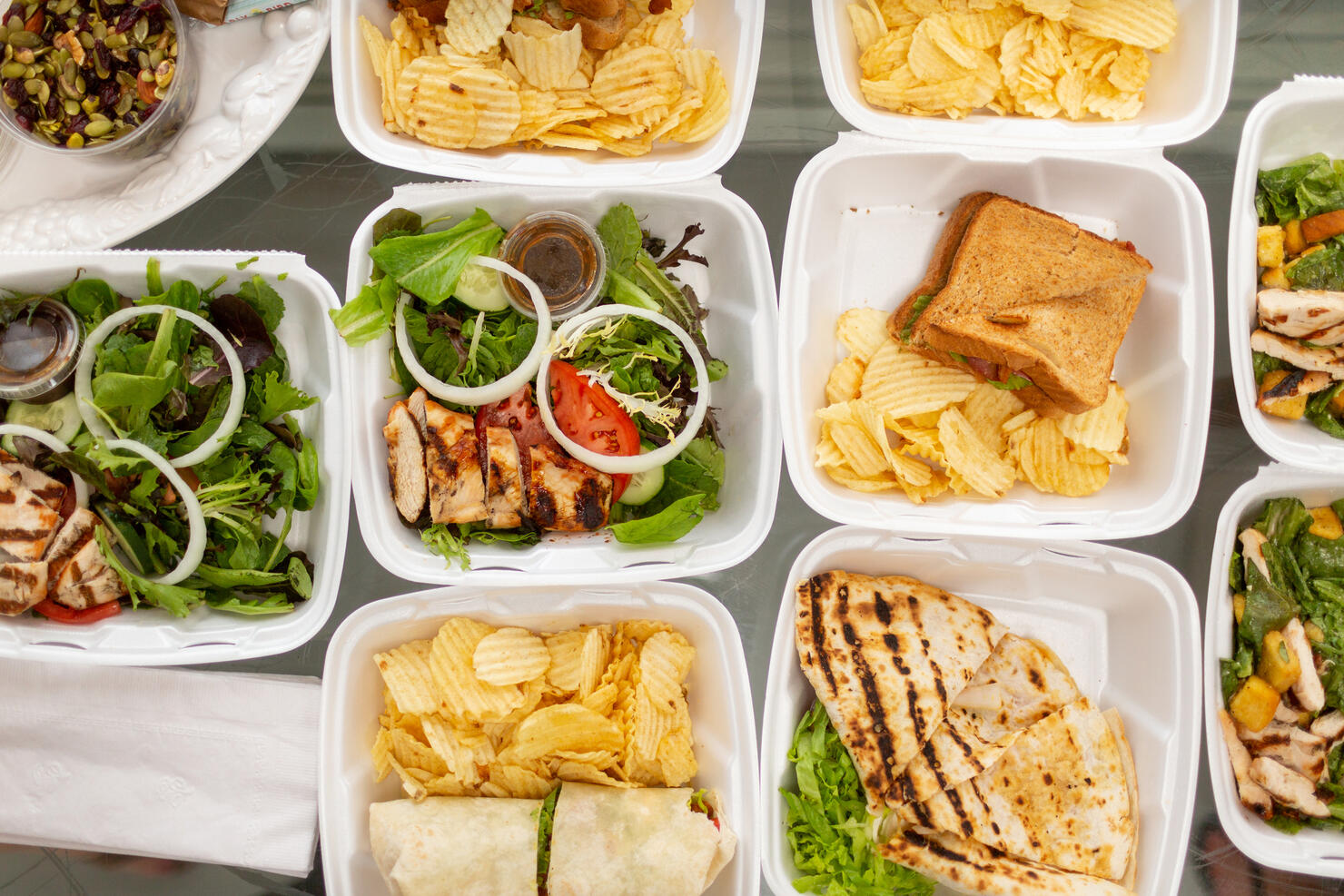 Takeout food and containers full of sandwiches, salads and potatoe chips