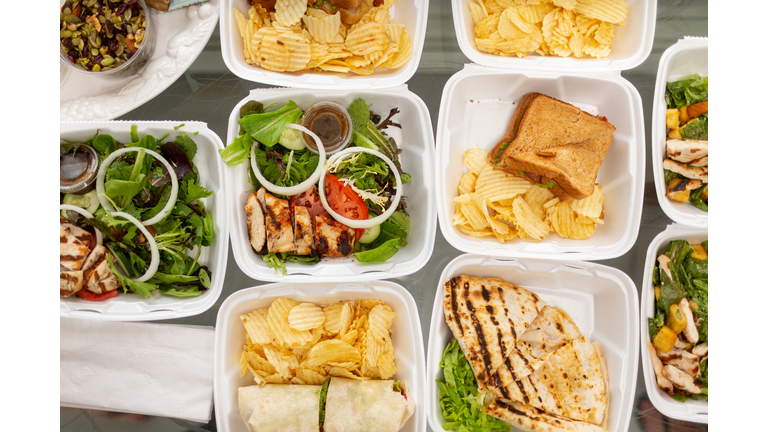 Takeout food and containers full of sandwiches, salads and potatoe chips