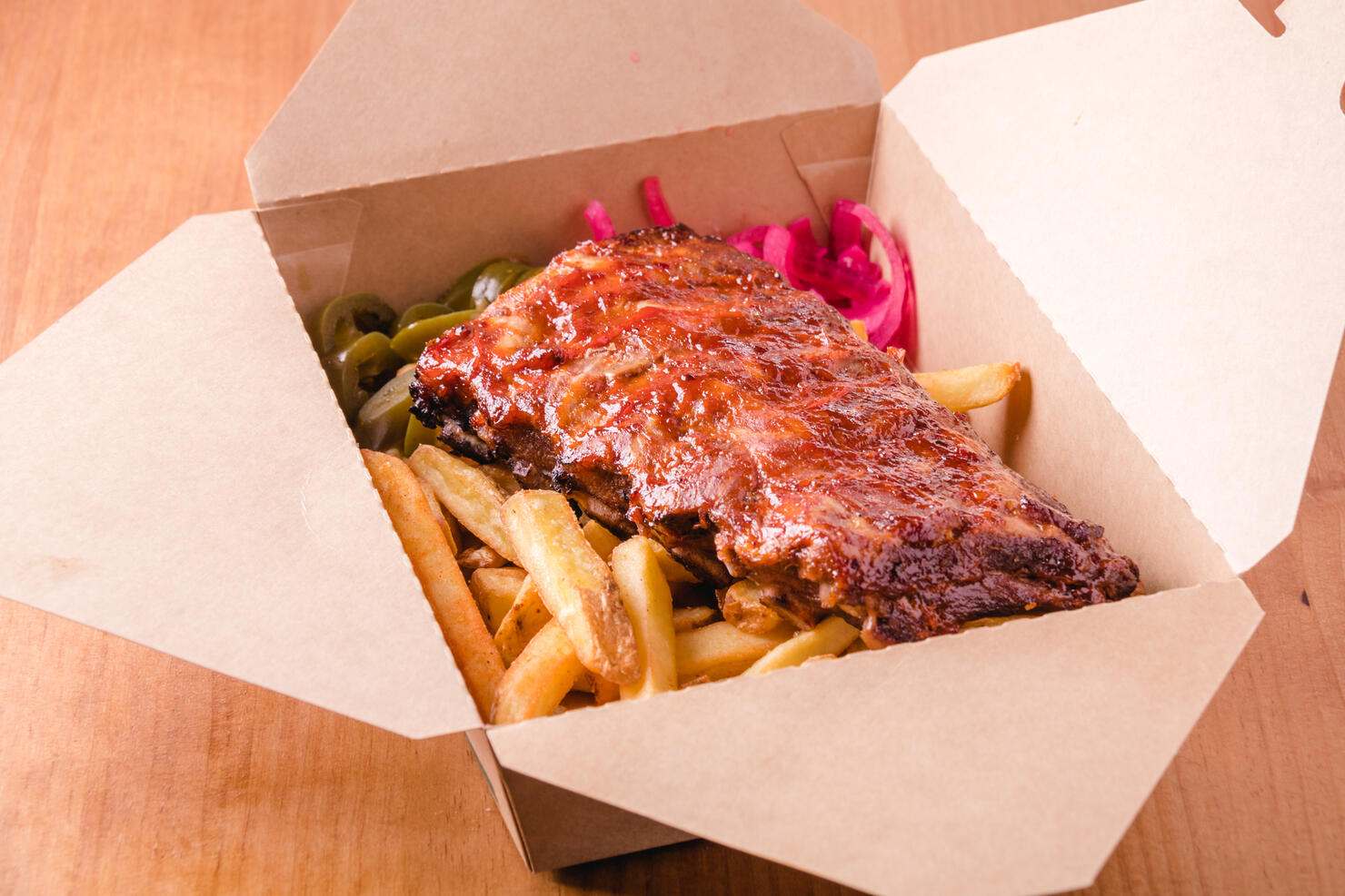Spicy hot grilled spare ribs from a BBQ served with french fries ready to take away