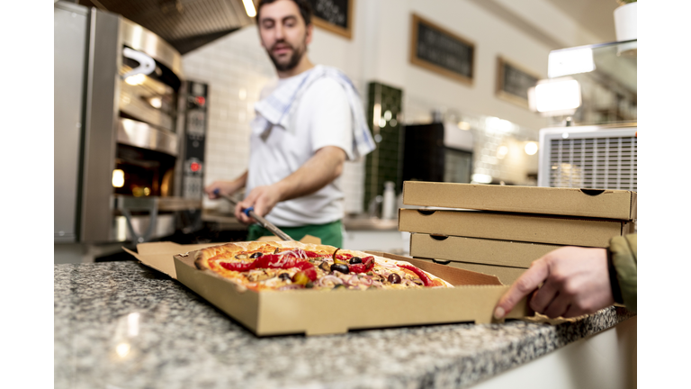 Pizzaiolo at work - chef is shovelling the pizza out of the oven into the pizza box