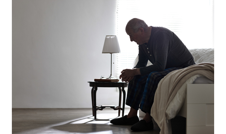 Elderly man sitting on bed looking serious