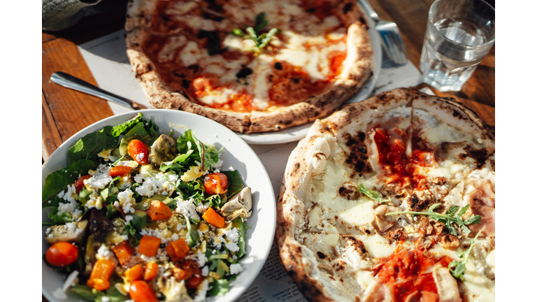 Elevated view of fresh pizza and green salad served on the table at outdoor restaurant