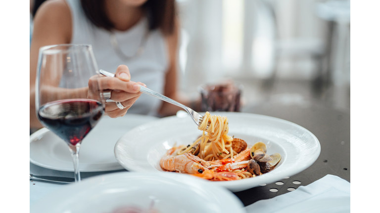 Close-up of young woman eating fresh seafood pasta in restaurant