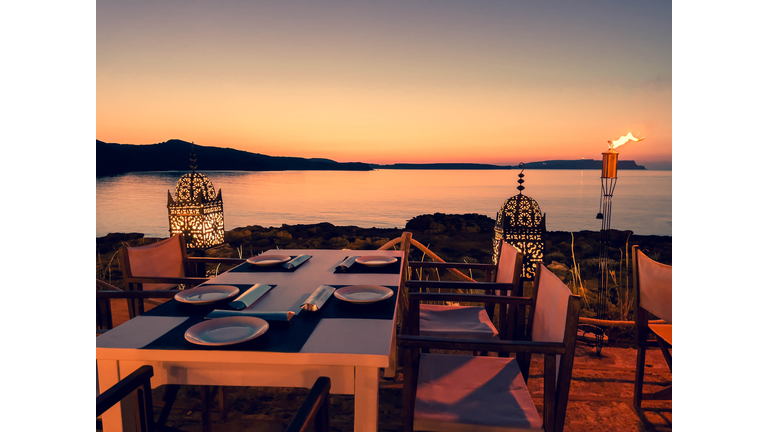 Romantic table for diner next to the sea with beautiful sunset sky.