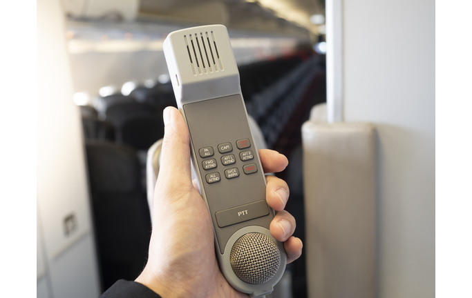 Male cabin crew holding interphone in aircraft cabin.