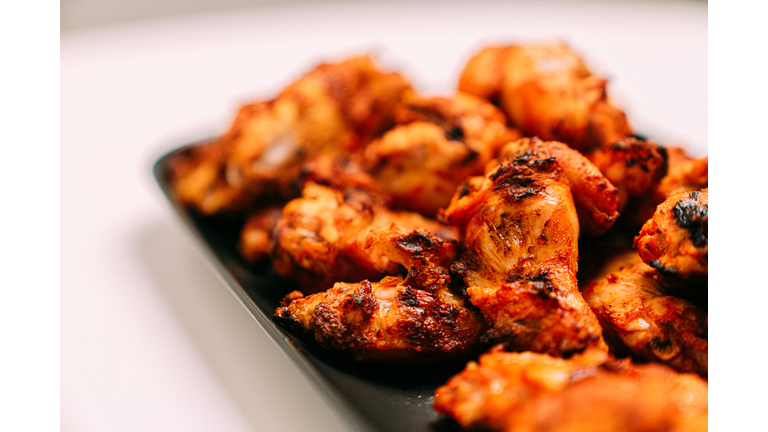Close-Up Copy Space Shot of Charring on Grilled Spicy Buffalo Chicken Wings on a White Table and Dark Gray Plate