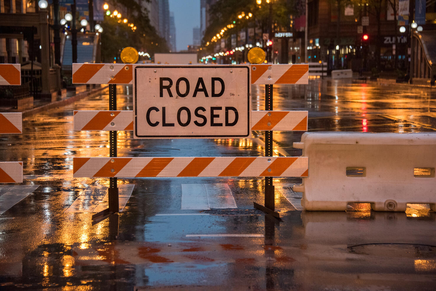 Road closed sign with colourful stop lights and traffic lights reflected on wet road