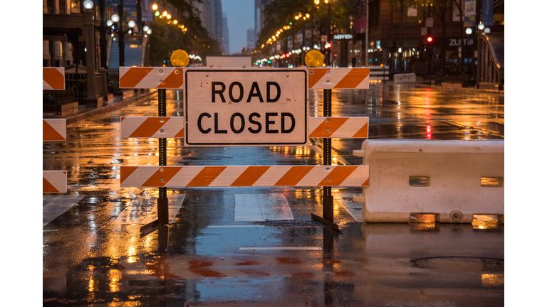 Road closed sign with colourful stop lights and traffic lights reflected on wet road