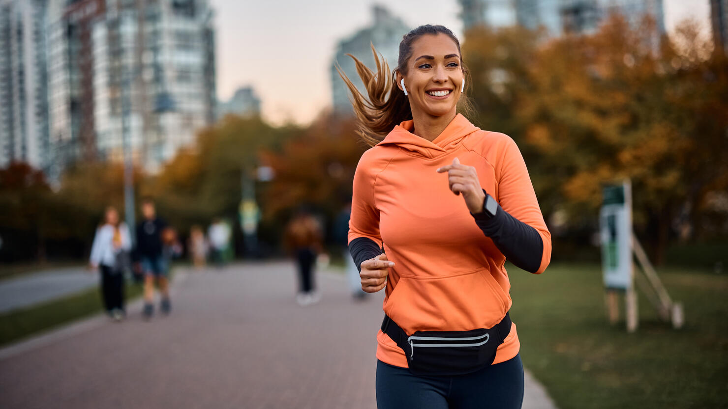 Happy sportswoman with earbuds running in the park.