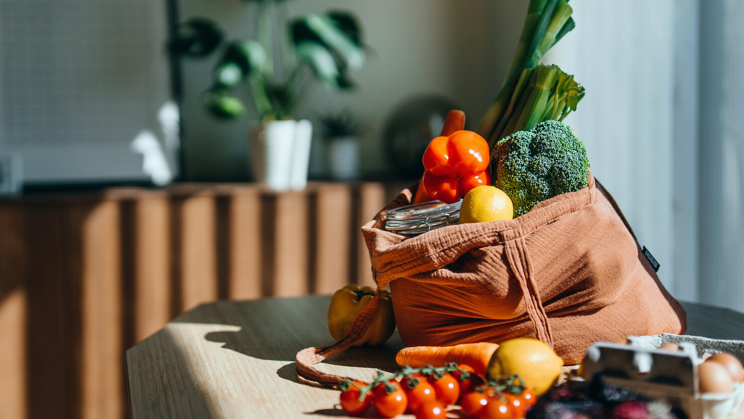 Eco-friendly reusable shopping bag with multi-coloured fresh vegetables and groceries on the table at home. Shopping with reusable grocery bag for plastic free and waste-free life. Responsible shopping. Zero waste and sustainable lifestyle concept