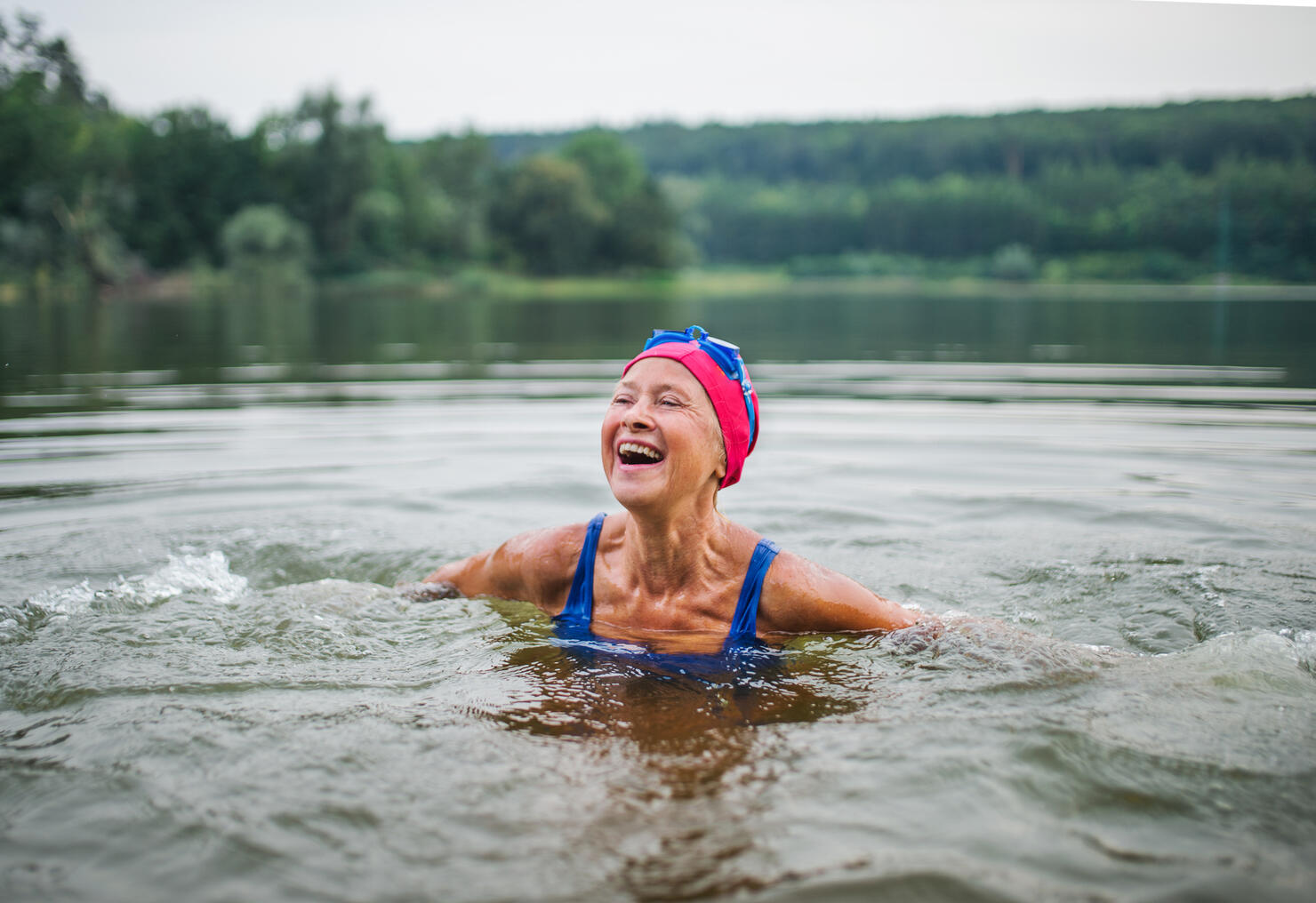 Active senior woman standing in lake outdoors in nature, laughing.