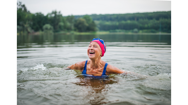 Active senior woman standing in lake outdoors in nature, laughing.