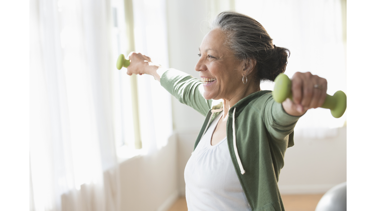 Older Hispanic woman lifting weights in living room