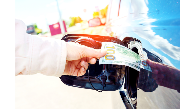 Expensive fuel concept. Rise in fuel price. Hand inserting a hundred dollar bill into the gas tank flap of a car.