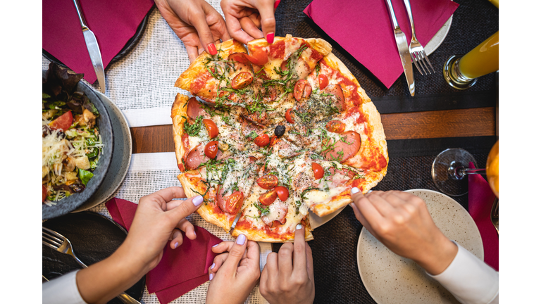 Young women taking a slice of pizza each at a restaurant