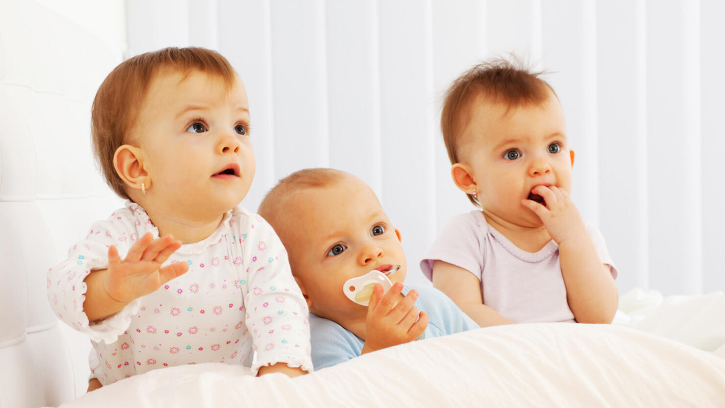 Beautiful baby triplets laying in their bed.