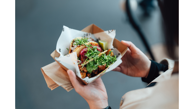 Young woman taking lunch break and enjoying tacos in street food market