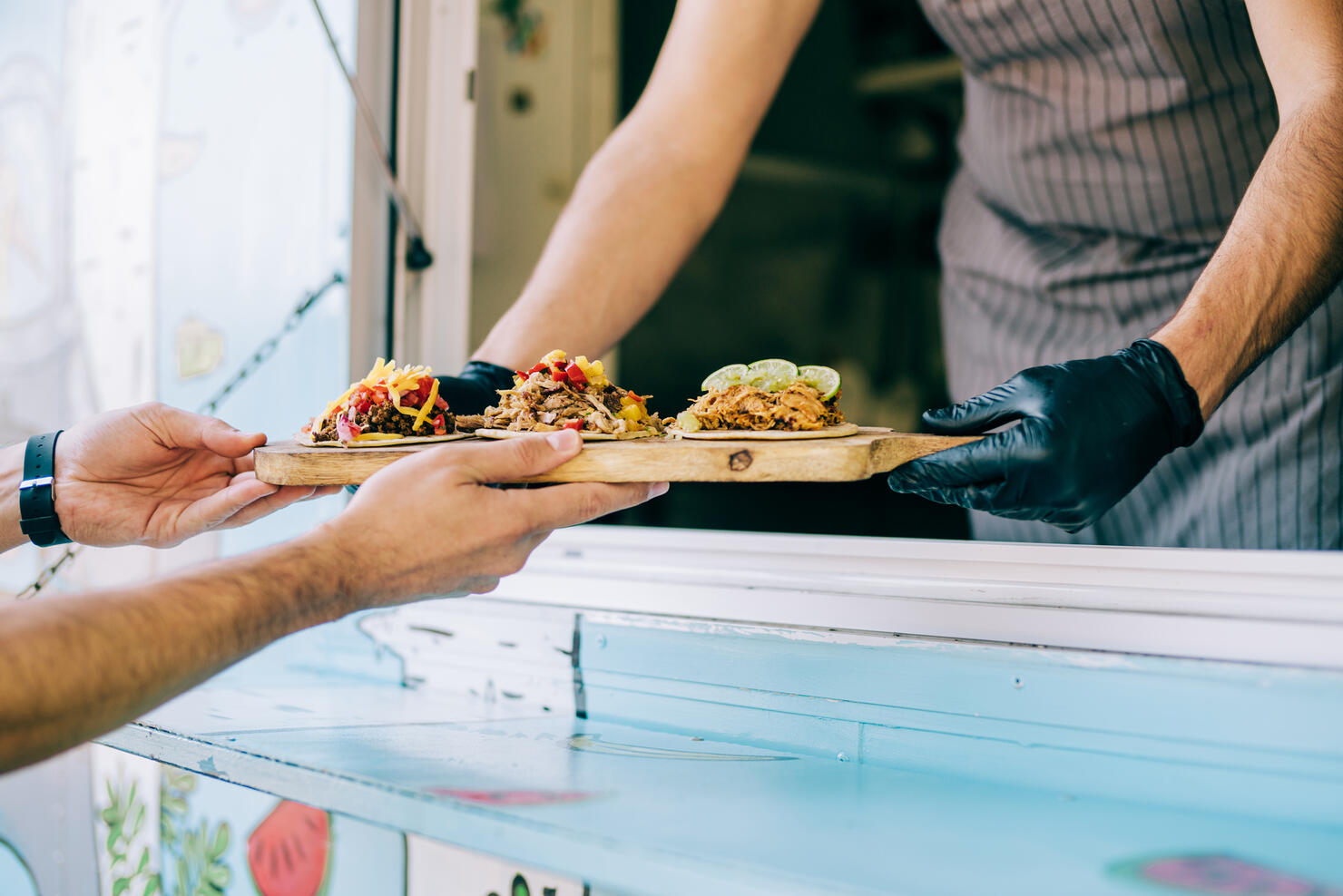 Food truck owner serving tacos to male customer.