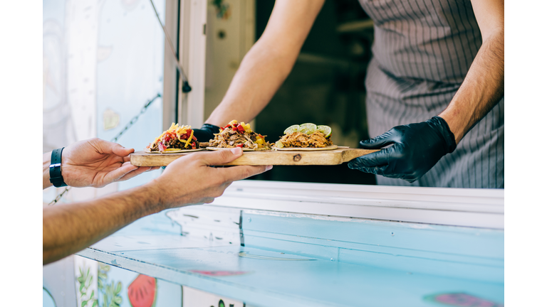 Food truck owner serving tacos to male customer.