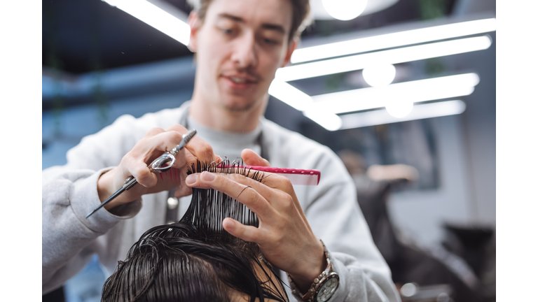 Experienced male beautician cutting teenage boy hair in contemporary stylist shop