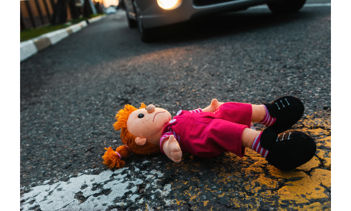 A sad plush toy doll is lying on the road near the wheel of a car. The concept of a road traffic accident