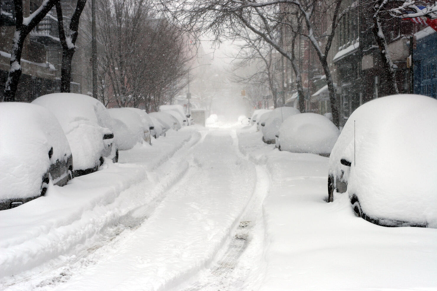 Looking down a road full of snow covered cars 