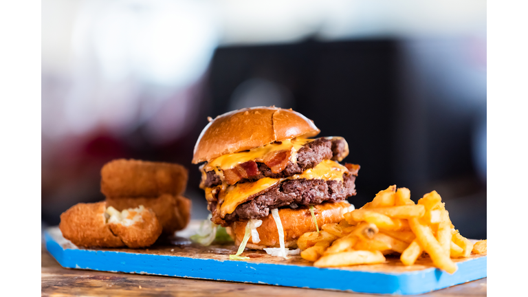 Burger greasy stacked street food, fried french fries closeup, melted cheese and bun on blue tray display in restaurant closeup, breaded fish sticks, bacon
