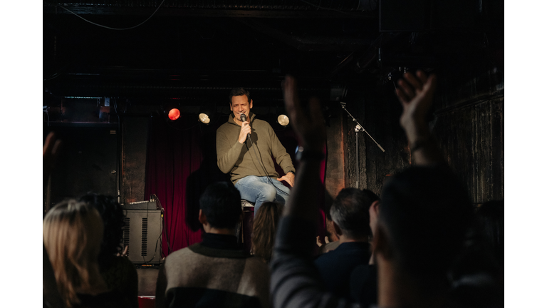 Senior male comedian performing in front of audience on stage at theater