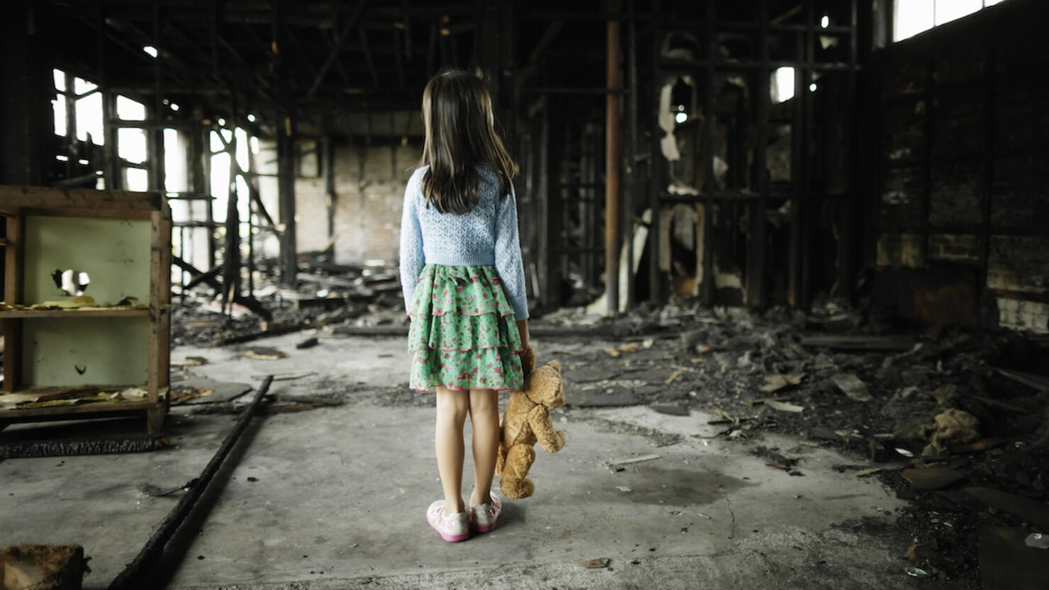 Girl with teddy bear in burned building