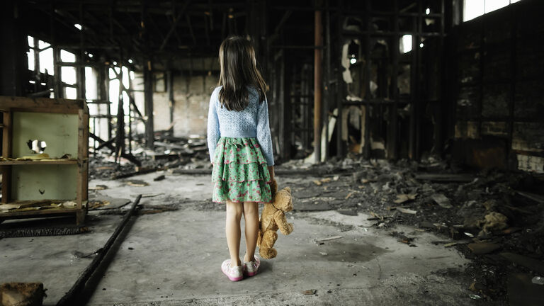 Girl with teddy bear in burned building